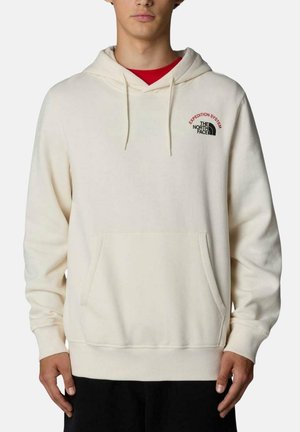 Sudadera beige con un bolsillo frontal, cordones y puños de canalé. Presenta un pequeño logo rojo y negro en el pecho. Textura suave.