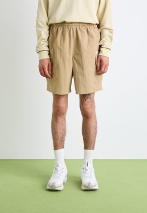 Beiga shorts med elastisk midja och sidofickor, i lätt material och med en ren design. Matchas med vita träningsskor och strumpor.