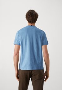 Jasnoniebieska bawełniana koszulka z okrągłym dekoltem i krótkimi rękawami; posiada mały pionowy pasek akcentujący na tylnym dekolcie.