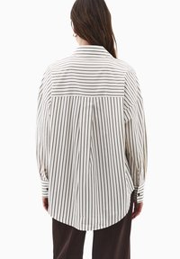 Gestreiftes Hemd in Weiß und Dunkelbraun. Verfügt über lange Ärmel, einen geraden Rücken und einen abgerundeten Saum. Glattes Material mit einer legeren Passform.