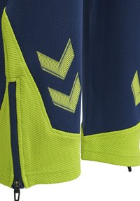 Close-up van marineblauwe en felgroene stof met een gestructureerd patroon, gele chevrons en een zwarte ritssluiting op de zijnaad van het kledingstuk.