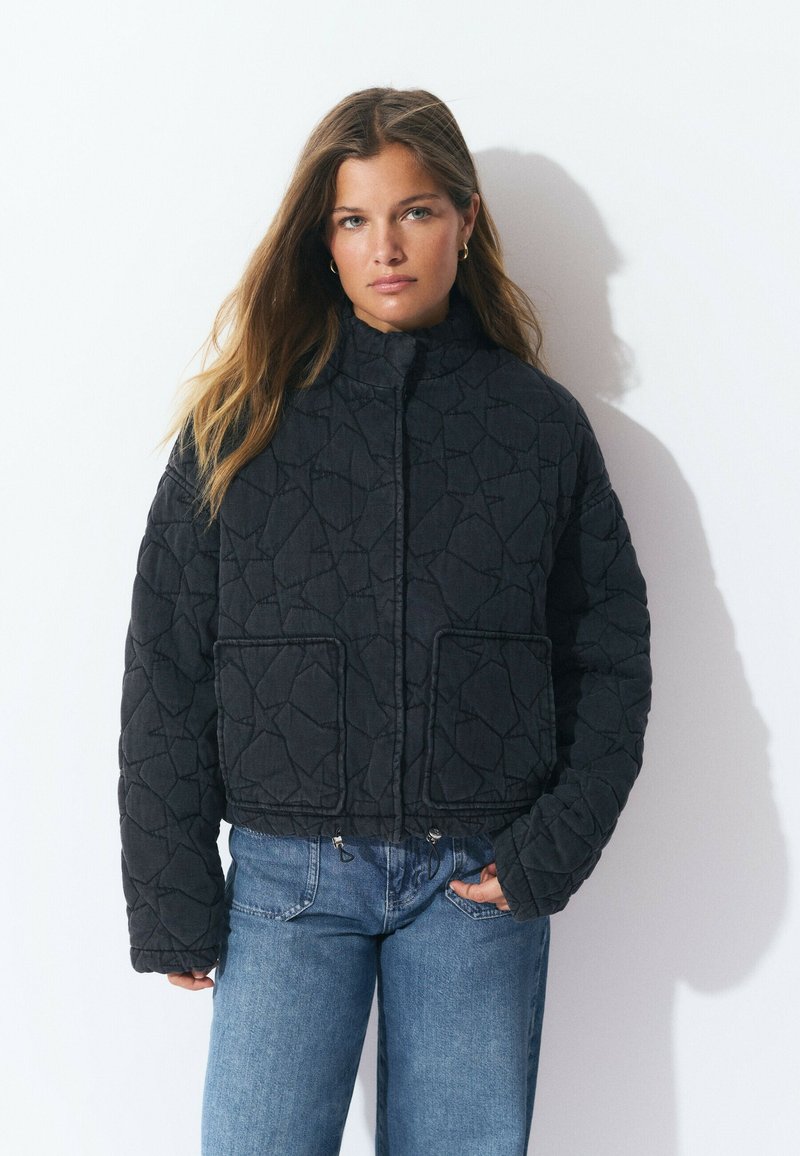 Veste noire matelassée avec un col haut, deux poches avant et un design court. La texture présente un motif géométrique.