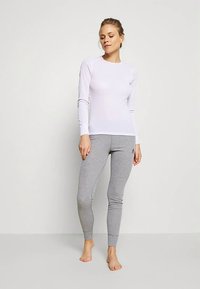 Langärmliges weißes Sportoberteil kombiniert mit grauen Leggings. Das Oberteil hat eine eng anliegende Passform, während die Leggings eine enganliegende, dehnbare Textur aufweisen.