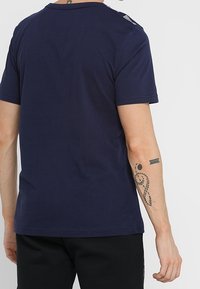 Námořnická modrá bavlněná trička s krátkým rukávem, kulatým výstřihem a bílými detaily na rameni. Hladká textura, volný střih.