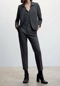 Traje gris a medida que presenta un blazer ajustado con cuello muesca y bolsillos frontales, combinado con pantalones slim. Textura mate, silueta elegante.