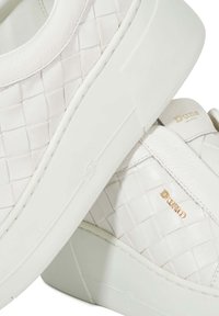 White leather sneakers featuring a woven texture, thick rubber sole, and gold logo accents. The design includes smooth and patterned sections.