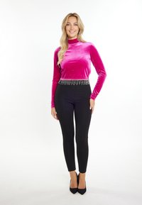 Fuchsia-farbenes Samtoberteil mit langen Ärmeln und einem mit Juwelen verzierten Saum an der Taille, kombiniert mit schwarzen, körperbetonten Hosen und spitzen schwarzen High Heels.