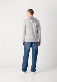 Sudadera gris con capucha ajustable, puños y dobladillo acanalados, combinada con jeans de mezclilla azules de corte holgado, luciendo con zapatillas blancas.