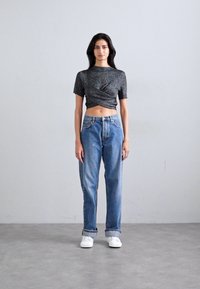 Svart och grå kortärmad crop top med vridet framstycke, matchad med högmidjade ljusblå jeans och vita sneakers.