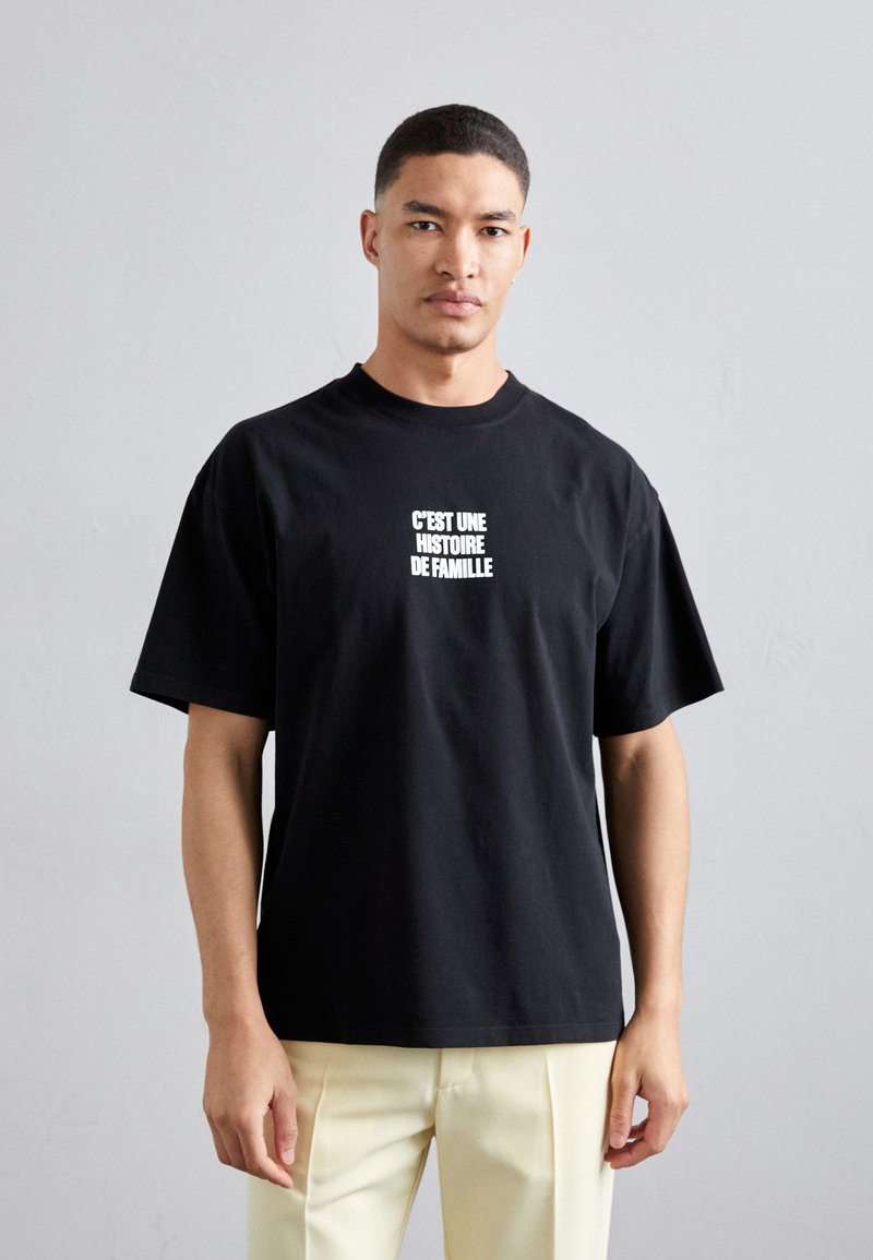 Sort T-shirt i bomuld med korte ærmer, prydet med hvid tekst på forsiden der står "C'EST UNE HISTOIRE DE FAMILLE." Simpelt, afslappet snit.