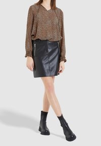 Blouse à imprimé animal brun avec des manches longues, associée à une mini jupe en cuir noir avec des zips sur les côtés. Des bottines noires à la cheville complètent la tenue.
