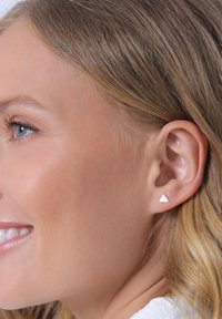 Silberne dreieckige Ohrstecker mit einer glatten Oberfl äche und minimalistischen Design. Auf dem Ohr eines Modells platziert, um die Form des Ohrrings zu zeigen.