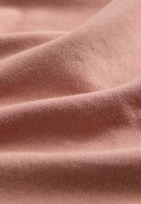 Jasnoróżowy dzianinowy materiał o drobnej fakturze i miękkich fałdach. Materiał wydaje się gładki z delikatnym połyskiem, podkreślającym jego rozciągliwość.