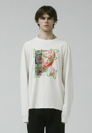Long-sleeve cream shirt featuring a graphic print in black, red, and green with abstract elements and text accents. Soft cotton fabric.