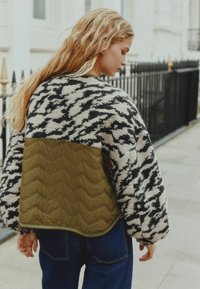 Kootud sviiter must-valge houndstooth mustriga varrukatel ja tekstuuriga oliivroheline tikand seljal. Üksikasjalik lõige, ümar hem.