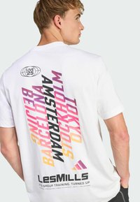 Camiseta blanca de manga corta con nombres de ciudades coloridos en tipografía negrita en la parte trasera, con un logotipo redondo arriba y el texto de la marca abajo.