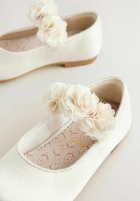 Ballerines blanches en satin avec un bout arrondi, ornées d'un cluster de fleurs en tissu sur la bride et d'une semelle intérieure à motif.
