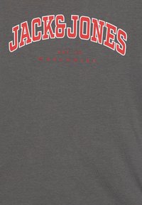 T-shirt en coton gris avec le logo "JACK&JONES" en texte rouge en gras, accompagné de "EST. 90" et "WORLDWIDE" en dessous en police rouge plus petite. Texture douce.