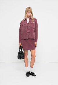 Σετ από βελούδινη ροζ σακάκι και μίνι φούστα με μπροστινές τσέπες και κλείσιμο με κουμπί. Αναδεικνύεται με μαύρη τσάντα χειρός και λόφερ.