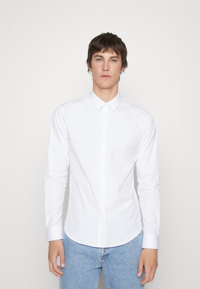 Hvit langermet skjorte med krage, laget av glatt stoff, med slim fit og avrundet hem, kombinert med lyseblå jeans.