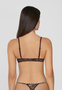 Soutien-gorge en dentelle et en mesh de couleur violet foncé avec des bretelles réglables et une fermeture à crochets. Il est orné de motifs floraux et est accompagné d'un string assorti.