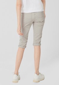Pantalones capri gris claro con puños enrollados, con bolsillos traseros y una textura suave. Combinados con zapatillas blancas para un look casual.