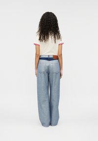 Παντελόνια από τζιν ανοιχτού μπλε χρώματος με άνοιγμα φαρδύ στο τελείωμα και καφέ δερμάτινο ταμπελάκι στη μέση πίσω, σε συνδυασμό με κρεμ κοντομάνικο πουκάμισο με ροζ λεπτομέρειες.