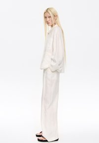 White linen oversized shirt and matching wide-leg pants, featuring minimalist design and subtle stitching details. Black sandals with accents.