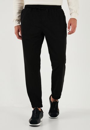 Black jogger pants with an elastic waistband, cuffed ankles, and a lightweight fabric, paired with black athletic shoes.