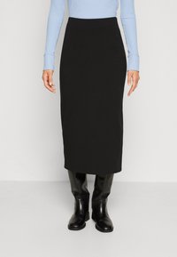 Schwarze Midirock in taillierter Form, mit glatter Textur und elastischem Bund, kombiniert mit kniehohen schwarzen Stiefeln und einem hellblauen Oberteil.