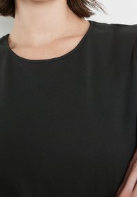 Haut noir à manches courtes en tissu lisse avec un décolleté rond, présentant un design épuré sans motifs ni accents visibles.