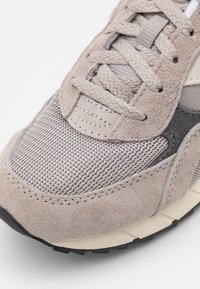Sneaker grigio chiaro con una combinazione di materiali in camoscio e rete, superficie testurizzata e suola in gomma nera con cuciture dettagliate.