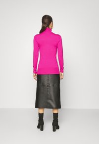 Fitted pink turtleneck sweater, ribbed cuffs, paired with a black leather midi skirt featuring a seam detail and chunky heeled black boots.