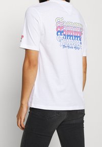T-shirt en coton blanc avec un graphic "Tommy" multicolore au dos, en rose, bleu et jaune, avec un col rond classique.