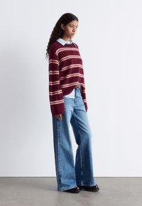 Burgunder gestreifter Strickpullover mit lockerer Passform, kombiniert mit weit geschnittenen hellblauen Denim-Jeans. Glatte Textur, minimalistisches Design.