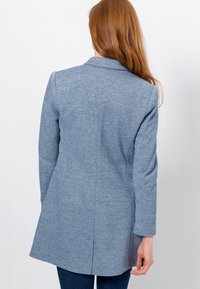 Vaaleansininen, teksturoitu takki, jossa on räätälöity muotoilu, yksirivinen etuosa ja pitkät hihat; siinä on sileä pinta ja takapilkku.