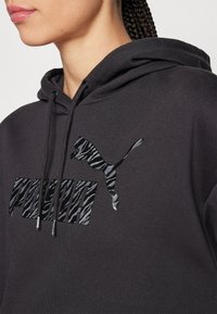 Sudadera negra de algodón, con un logotipo de Puma en estampado de cebra brillante. Se aprecian los cordones y una textura suave.