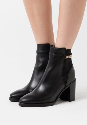 Bottes chevilles en cuir noir avec un bout pointu et un talon bloc. Elles présentent un accent en métal doré et une silhouette élégante.