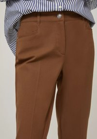 Pantaloni marroni su misura con una texture liscia, dotati di chiusura frontale con zip e bottone, tasche laterali e dettagli di pieghe per un finish elegante.