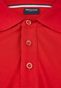 Polo rouge en tissu texturé, avec trois boutons assortis et un col rayé contrasté. Étiquette de marque : Hechter Paris.