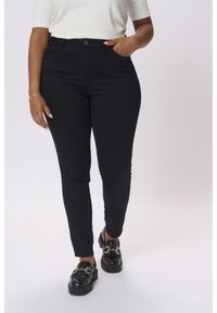 Jean noir taille haute en denim, dotée d'une coupe slim, de poches avant et d'une fermeture à bouton. Portée avec des mocassins noirs.