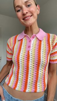 Knitirana polo majica z rožnatimi, oranžnimi, rumenimi in belimi črtami. Kratki rokavi, z gumbnim ovratnikom in odprtimi detajli po vsej majici.