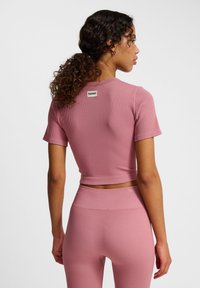 Roze geribbelde crop top met korte mouwen, voorzien van een logootag aan de achterkant. De stof heeft een gestructureerde afwerking, die perfect past bij bijpassende leggings.