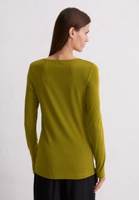 Top à manches longues en tissu côtelé vert olive atténué, avec un encolure ronde et une coupe décontractée, associé à un bas noir.