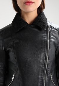 Czarna skórzana kurtka o teksturowanym wykończeniu, z kołnierzem z owczej wełny, zapinana na zamek błyskawiczny z przodu oraz z bocznymi kieszeniami.