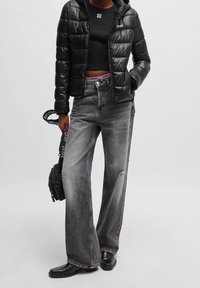 Svart dunjacka med huva, kort svart topp, grå vida jeans och svarta glansiga stövlar. Märkbara HUGO-logotyper och detaljer med remmar.