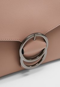 Rosa läderhandväska med ett klaffförslutning och dubbla metallringar som accent. Ytan har en mjuk textur med synliga sömnadsdetaljer.