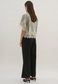 Top corto gris transparente con intrincado borde de encaje, combinado con pantalones negros de cintura alta y tacones abiertos. Textura suave, diseño ligero.