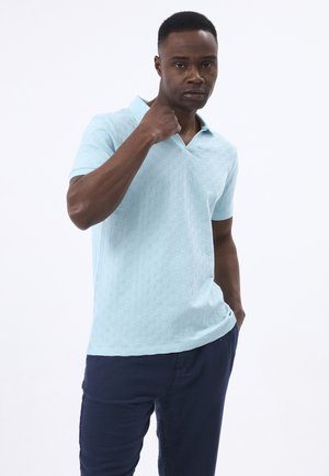 Polo shirt azzurro chiaro con un motivo a scacchi testurizzato, maniche corte e scollo a V, indossato sopra pantaloni navy scuri.