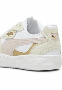 Zapatilla blanca con acentos en beige y rosa claro. Cuenta con materiales de ante y sintéticos, logo dorado, cuello acolchado y suela blanca texturizada.